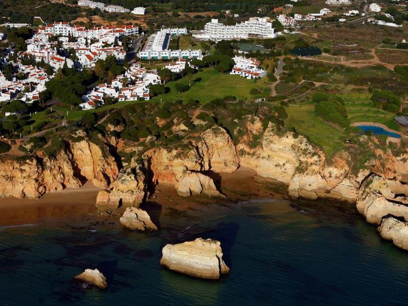 Costa con rocce, acqua blu e edifici bianchi in un paesaggio verde.