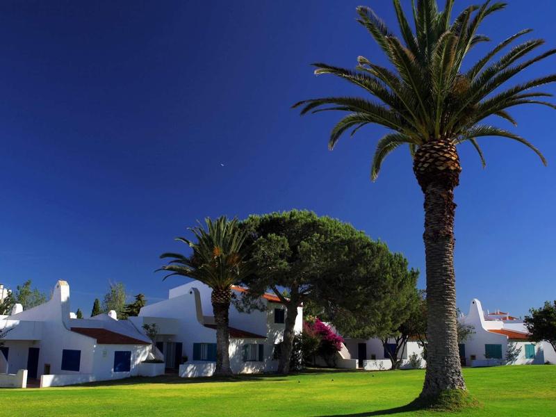 Casa vacanze bianca con palme e prato verde sotto un cielo blu limpido.