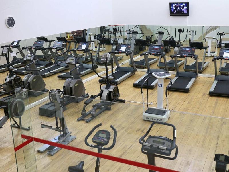 Ampia palestra con file di ellittiche, tapis roulant e cyclette su pavimento in legno.