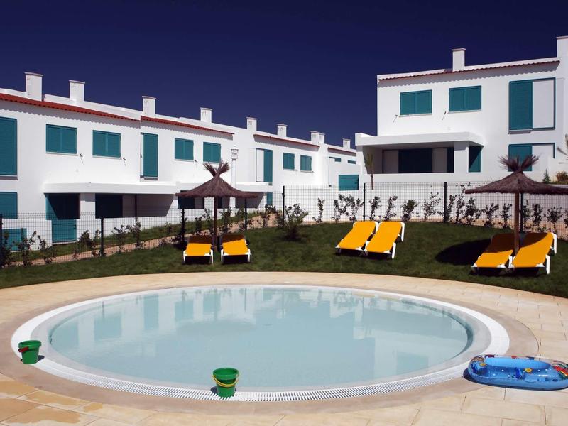 Piscina rotonda con lettini davanti a case vacanza bianche sotto un cielo terso.