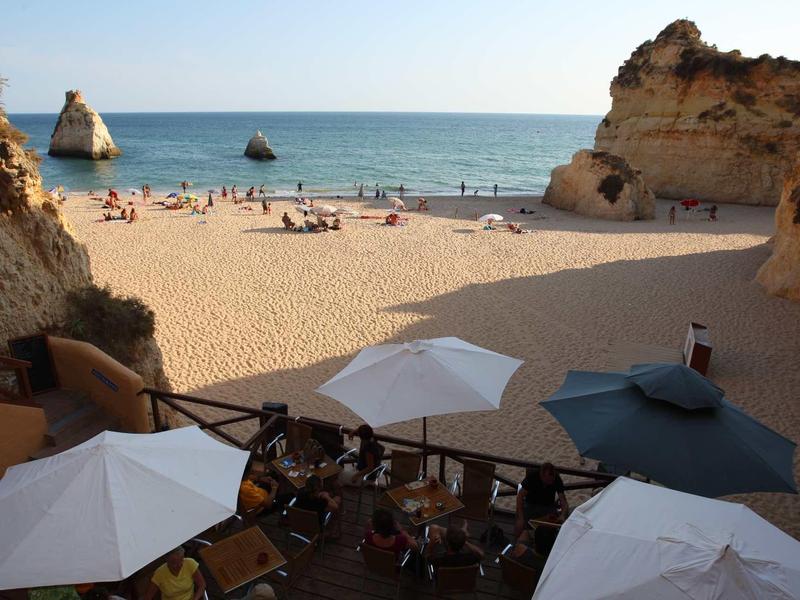 Spiaggia sabbiosa tra scogliere con ombrelloni e vista sul mare sullo sfondo.