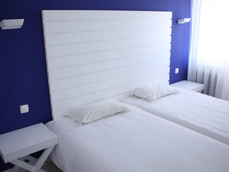 Due letti singoli con lenzuola e cuscini bianchi davanti a una parete blu e una testiera bianca.