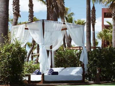 Luxuriöses Himmelbett mit weißen Vorhängen neben einem Pool und Palmen.