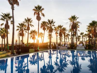 Sonnenuntergang über einem Pool mit hohen Palmen in einem Hotelresort.