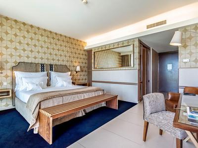 Modernes Hotelzimmer mit großem Bett, dekorativem Teppich und Sitzbereich mit Tisch und Stuhl.
