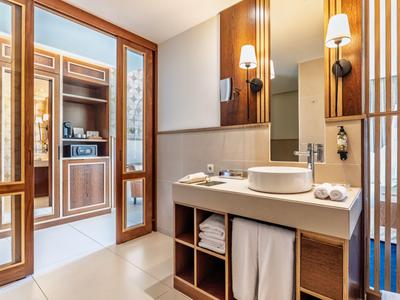 Modernes Badezimmer mit Waschbecken, Holzregalen und Glaswand zu einem Schlafzimmer.