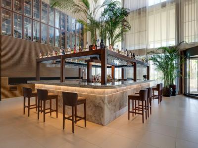 Moderner Hotelbarbereich mit Marmortresen, hohen Stühlen und großen Pflanzen.