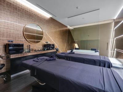 Moderner Hotel-Wellnessraum mit zwei Massageliegen, Spiegeln und schlichter Beleuchtung.