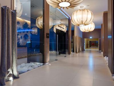Moderner Hotelgang mit großen Glaswänden, eleganten Lampen und weichen Vorhängen in warmem Licht.