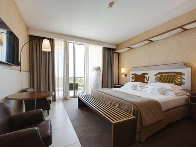 Modernes Hotelzimmer mit großem Bett, Tisch, Fernseher und Blick auf Balkon.