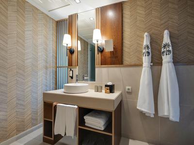 Modernes Hotelbad mit Waschbecken, Wandspiegel und zwei an der Wand hängenden weißen Handtüchern.