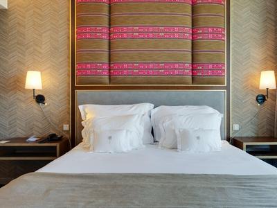 Modernes Hotelzimmer mit Doppelbett, weißen Kissen, zwei Nachttischen und stilvollen Wandlampen.