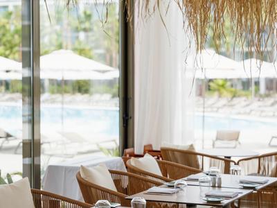 Sauber gedeckte Tische in einem hellen Restaurant mit Blick auf den Pool und natürlichen Dekorationen.