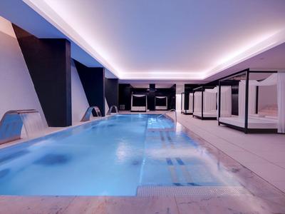 Moderner Innenpool mit Wasserfall und Liegen in einem Hotel.