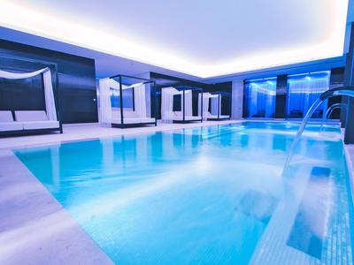 Moderne Spa-Lounge mit beleuchtetem Pool und Wasserfall, atmosphärisch in Blau- und Weißtönen.