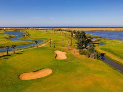 Grüner Golfplatz mit Sandbunkern, flankiert von Wasser unter blauem Himmel.