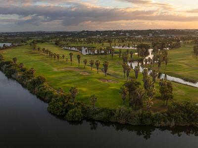 Grüner Golfplatz neben einem Fluss unter bewölktem Himmel bei Sonnenuntergang.