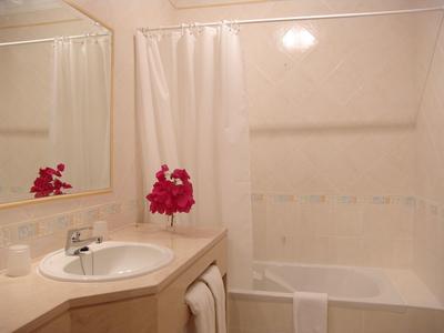 Jasna łazienka z umywalką, lustrem, wanną i różowymi kwiatami jako dekoracją.