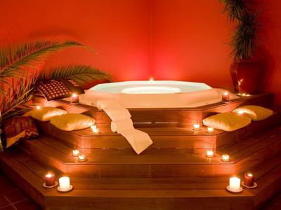 Jacuzzi w ciepło oświetlonym pokoju z świecami i poduszkami na drewnianym podeście.
