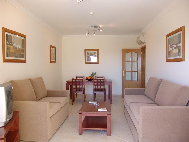 Jasny salon z dwoma sofami, szklanym stolikiem i stołem jadalnym z krzesłami w pokoju hotelowym.