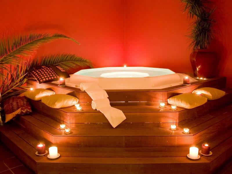 Jacuzzi w ciepło oświetlonym pokoju z świecami i poduszkami na drewnianym podeście.