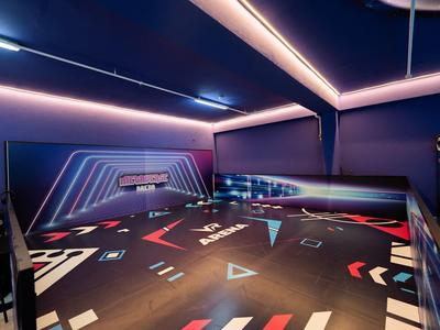 Una sala da bowling moderna con luci al neon colorate e pavimento scuro con motivi geometrici.