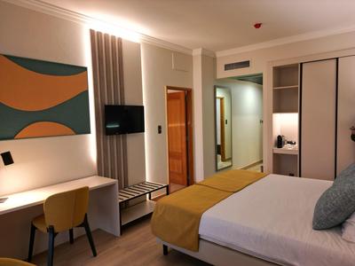 Camera d'albergo arredata modernamente con letto matrimoniale, scrivania e TV a parete.