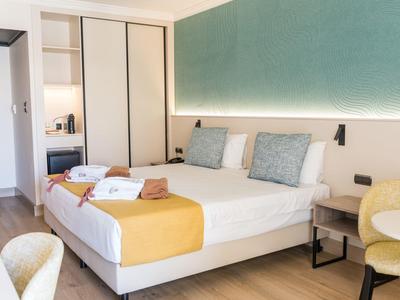 Camera d'hotel moderna con letto matrimoniale, illuminazione della testiera e pavimento in legno chiaro.