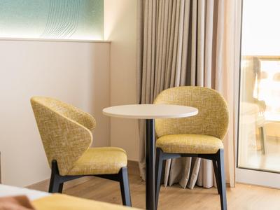 Piccolo tavolo rotondo con due sedie gialle in una stanza d'hotel luminosa accanto a tende e finestra.