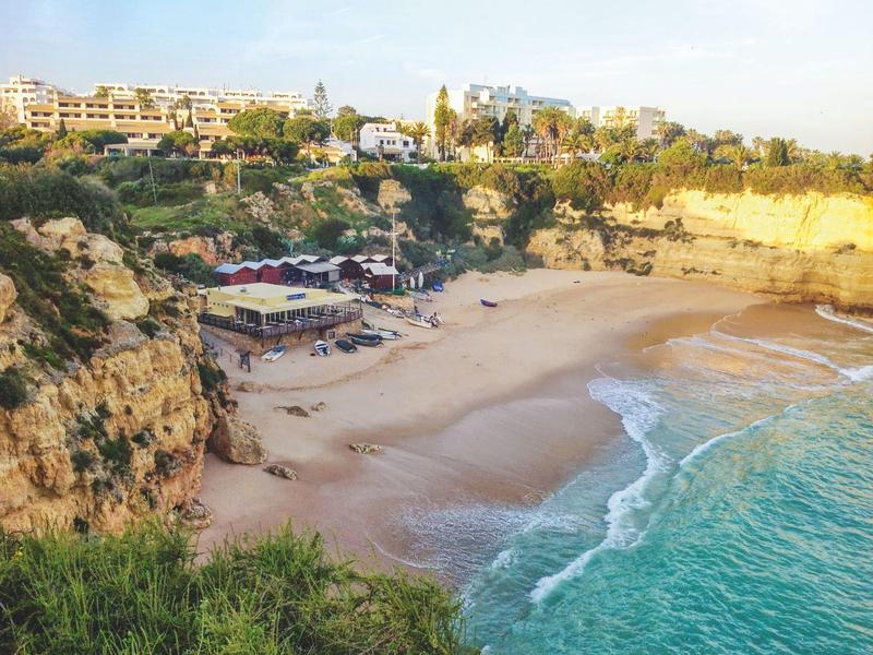 Spiaggia con scogliere, acqua turchese e edifici in lontananza sotto un cielo sereno.