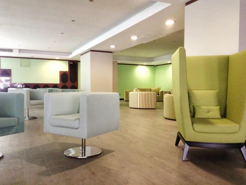 Zona lounge moderna dell'hotel con diverse poltrone comode in colori neutri e pavimento in legno.