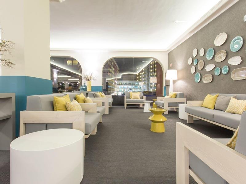 Lounge moderna con divani, tavoli rotondi e pannelli decorativi alle pareti in uno spazio luminoso e accogliente.