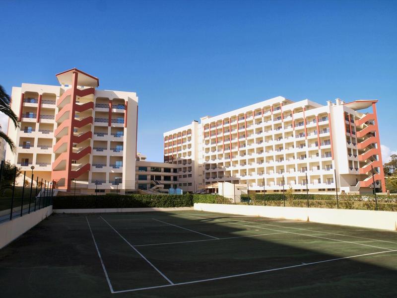 Edifici dell'hotel con campo da tennis di fronte sotto un cielo azzurro chiaro.