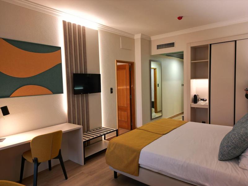 Camera d'albergo arredata modernamente con letto matrimoniale, scrivania e TV a parete.