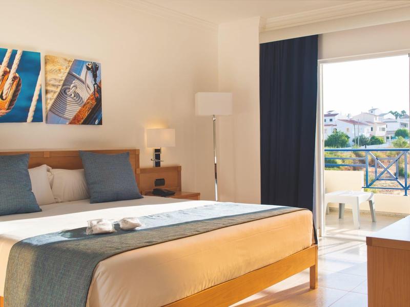 Camera d'hotel luminosa con letto grande, accenti blu e balcone con vista sulla città.