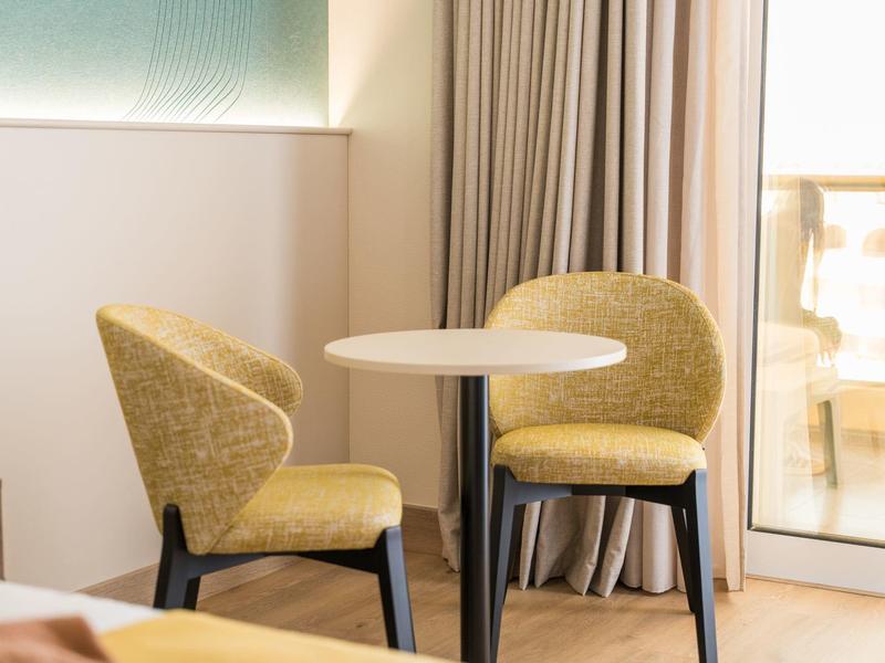 Piccolo tavolo rotondo con due sedie gialle in una stanza d'hotel luminosa accanto a tende e finestra.