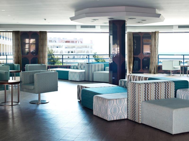 Area lounge moderna e luminosa dell'hotel con gruppi di sedute e grandi finestre che si affacciano all'esterno