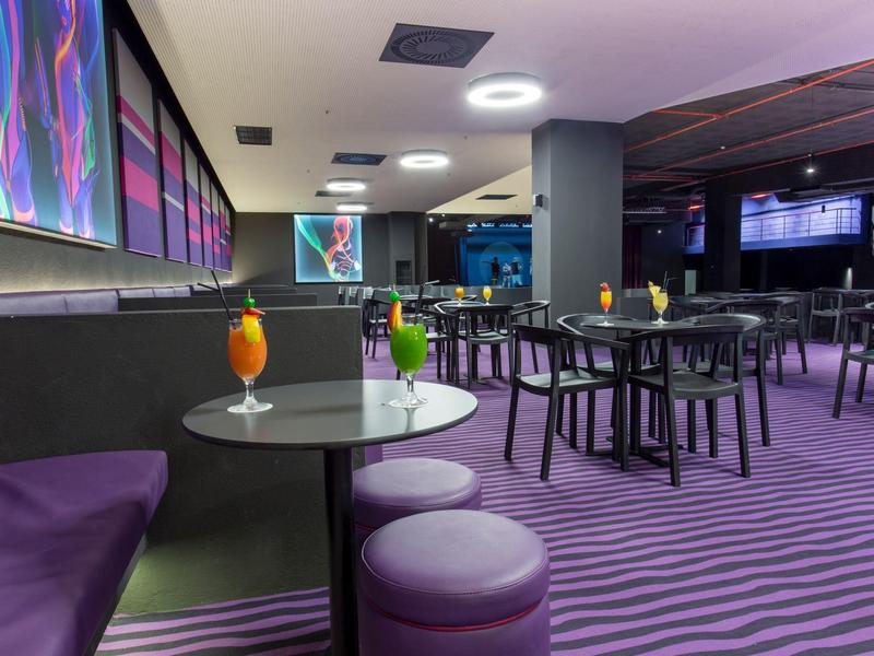 Bar dell'hotel moderna con moquette viola, tavoli rotondi, sedute e bevande decorative.