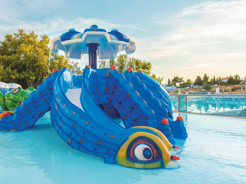 Scivolo d'acqua a forma di drago colorato in piscina poco profonda sotto il cielo azzurro.