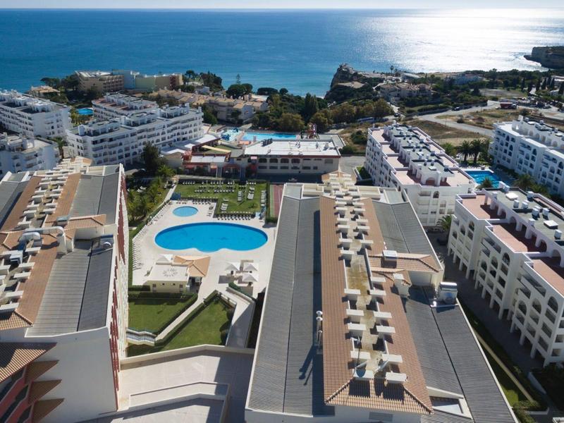 Vista aerea di un complesso alberghiero con piscina e vista sul mare all'orizzonte.
