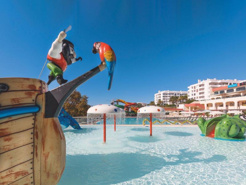 Parco acquatico con scivoli d'acqua, figure giocose e hotel sullo sfondo in una giornata di sole