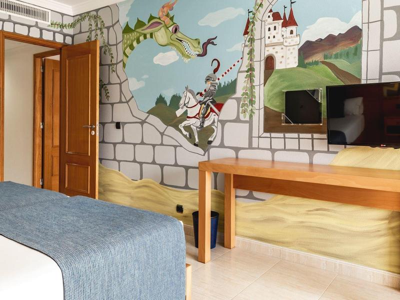 Camera d'hotel ben illuminata con murale colorata e TV a schermo piatto moderno sopra una scrivania in legno.