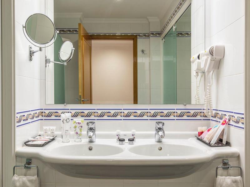 Bagno luminoso con lavabo, specchio, asciugacapelli e asciugamani accanto alla doccia.