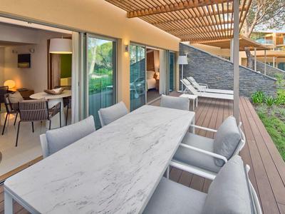 Terrazza con grande tavolo in marmo e sedie imbottite davanti a una camera d'hotel con vista mare.