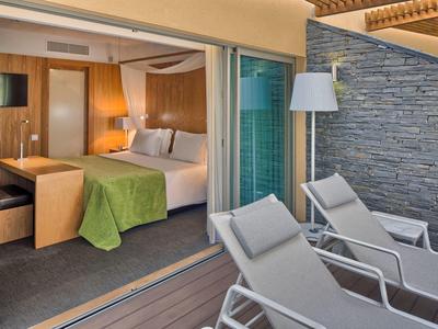 Camera d'hotel con letto matrimoniale, copriletto verde, scrivania e terrazza annessa con sdraio