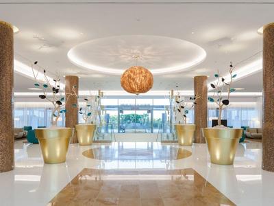 Elegante hall dell'hotel con lampadario dorato, colonne in marmo e aree salotto moderne.