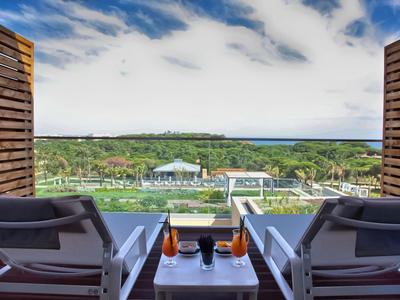 Vista da due lettini su paesaggio verde e mare, con bevande su un piccolo tavolo.