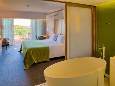 Camera d'hotel moderna con vasca da bagno, letto spazioso e vista sul paesaggio verde.