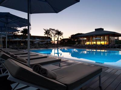 Vista serale di una piscina moderna con lettini e ombrelloni in un hotel.