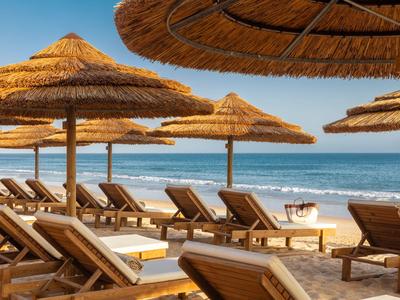 Strand mit Liegestühlen und Strohhut-Sonnenschirmen am Meer